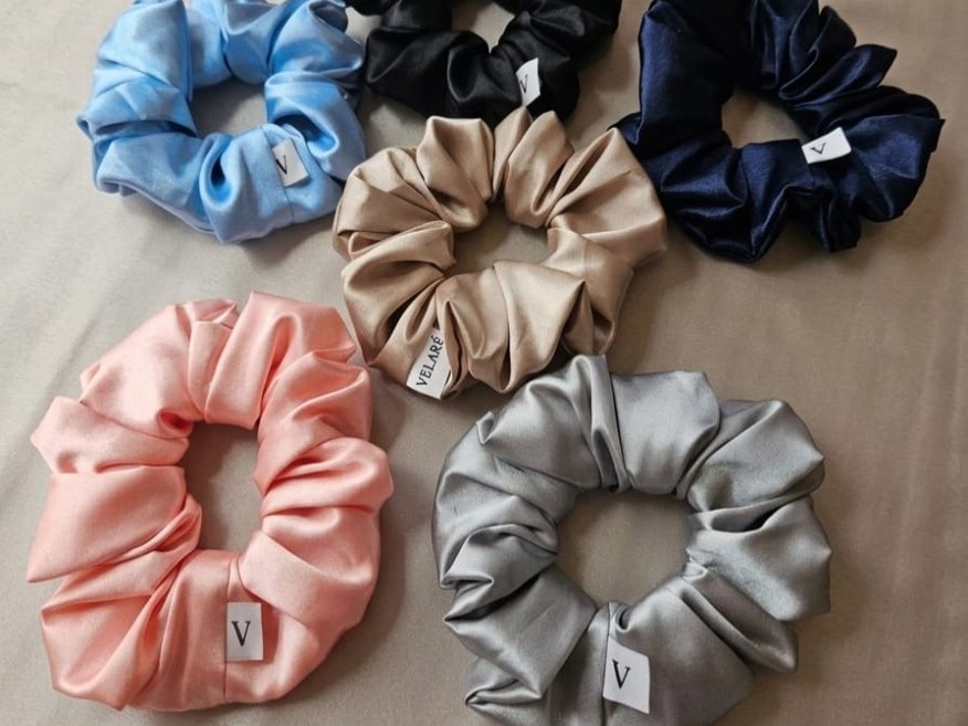 Six satin VELARÉ scrunchies in blue, black, navy, champagne, peach, and silver